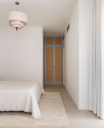 Minimalist bedroom with white bed, tiered pendant light, and cane wardrobe doors in blue-grey frame