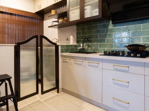 Kitchen with green subway tile backsplash, white cabinetry, brass handles, and a glass partition door