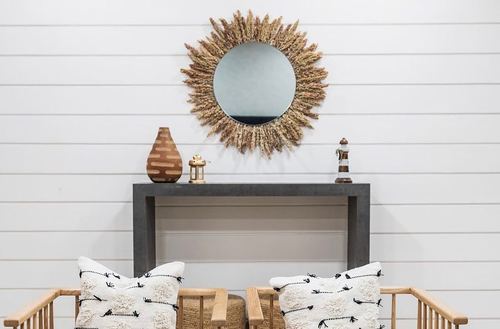 Shiplap wall with sunburst mirror over dark console table and patterned cushions on chairs
