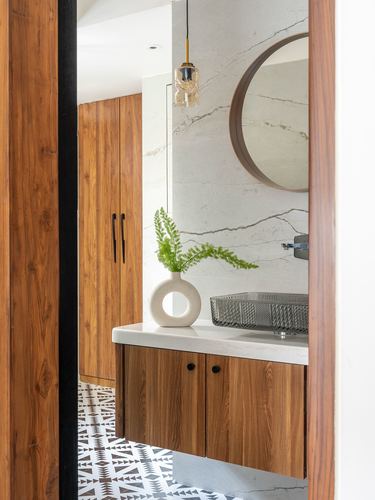 Wood-framed bathroom doorway revealing floating vanity, round mirror, and patterned tile floor