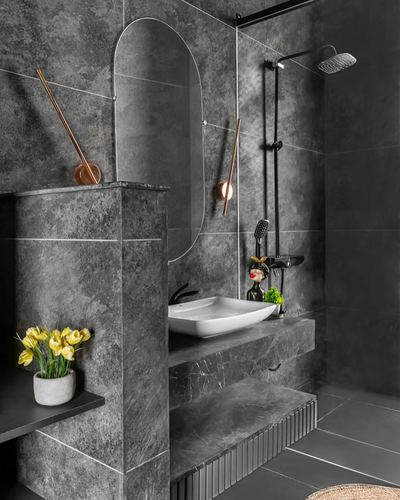Dark stone bathroom with oval mirror, vessel sink, black shower and yellow flowers
