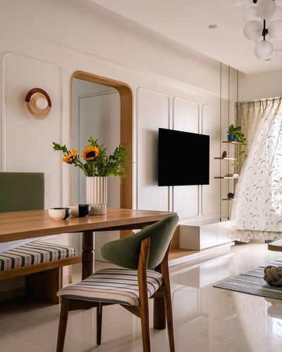 Dining table with striped bench and green chair beside arched mirror and tv wall panel