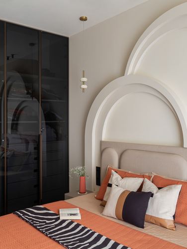Bedroom with arched plaster niches, upholstered headboard, orange pillows, and black glass wardrobe