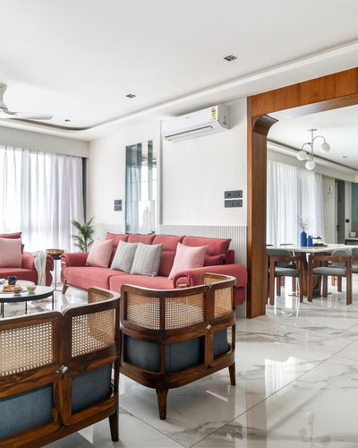 Living room with cane armchairs, pink sofa, marble floor, and wooden archway to dining area