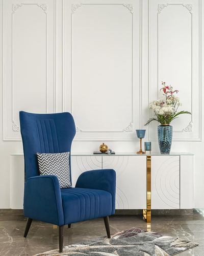Blue velvet wingback chair beside white console with brass legs and classical wall paneling