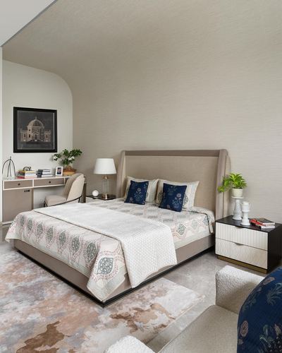 Neutral toned bedroom with upholstered wingback bed, black nightstand, and desk nook by window