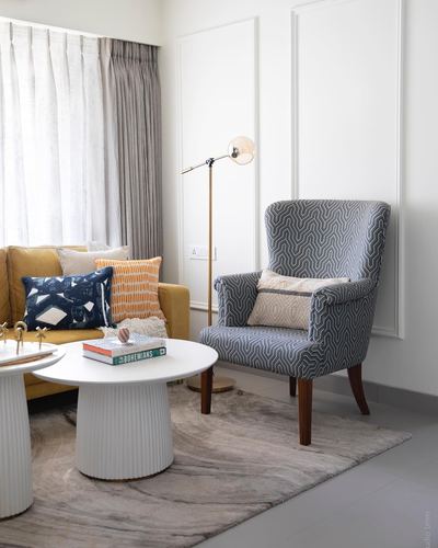 Living room corner with patterned wingback chair, mustard sofa, and fluted round coffee table on rug