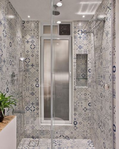 Shower stall fully clad in blue and white patterned tile with glass partition and frosted door