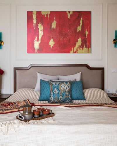 Neutral bedroom with wood-trimmed headboard, teal ikat cushions, and a red-gold abstract painting above.