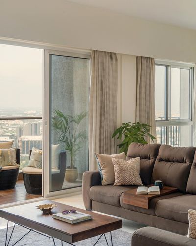 Living room with brown sofa, wooden coffee table, and balcony overlooking city skyline