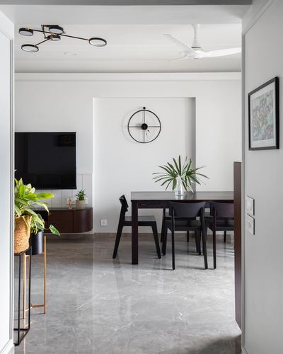 Dining area with dark wood table and chairs seen through a doorway, round clock set in a wall niche