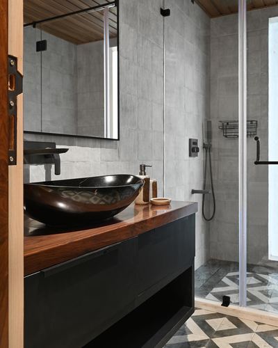 Bathroom with concrete walls, wood vanity, black boat-shaped sink, and glass-enclosed shower with patterned floor tile