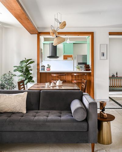 Charcoal velvet sofa in living room opening through wooden archway into mint-green kitchen