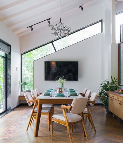 Dining room with wooden table, cane-backed chairs, sculptural chandelier and angled clerestory window