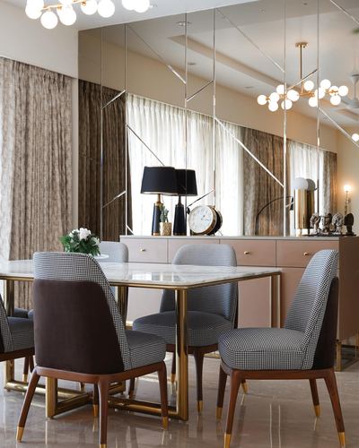 Dining room with marble-top table, houndstooth chairs and mirrored wall behind pink sideboard