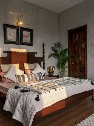 Bedroom with turned wood bed, textured grey plaster walls, and a carved wood and brass door