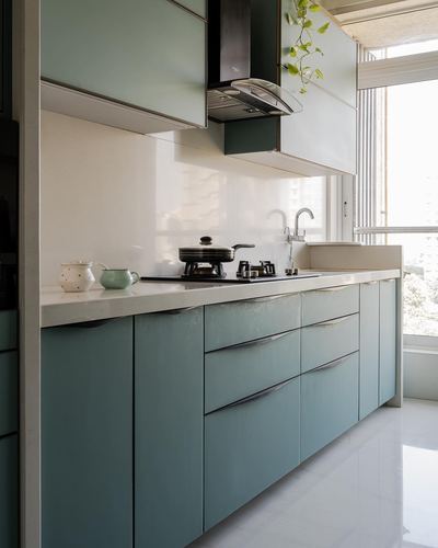 Galley kitchen with sage green glossy cabinetry, stone counter, gas hob and chimney hood, window at end
