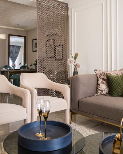 Living room with cream armchairs, taupe sofa, floral cushions, and a decorative metal screen divider