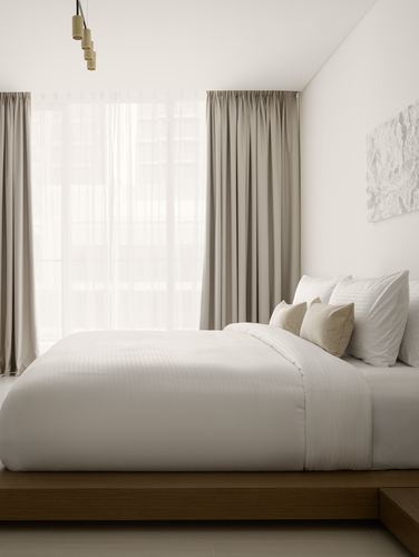 Minimalist neutral bedroom with wood platform bed, layered curtains, and abstract stone-like artwork