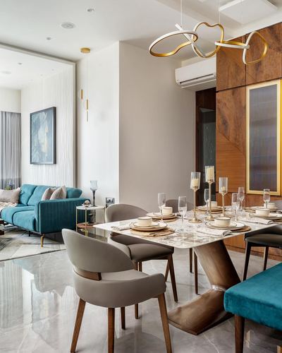 Dining table set with white and gold plates under sculptural gold pendant lights, teal sofa beyond