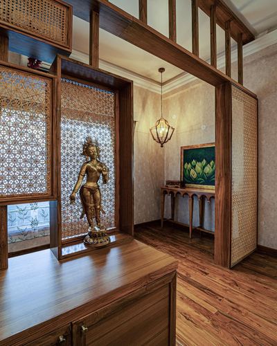 Wooden foyer with carved lattice screens, bronze deity statue, and hanging lantern leading to a console table