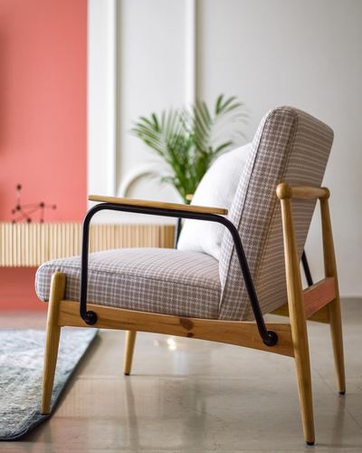 Mid-century wood armchair with houndstooth cushion beside coral wall and plant