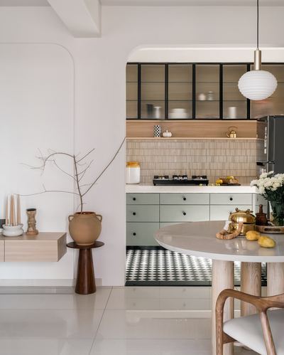 Arched opening reveals sage-green kitchen with checkerboard floor, glass cabinets, and round dining table in foreground