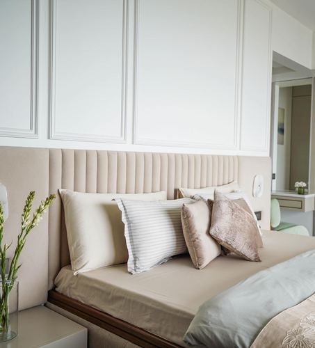 Beige channel-tufted headboard with layered pillows against white paneled wall in bedroom