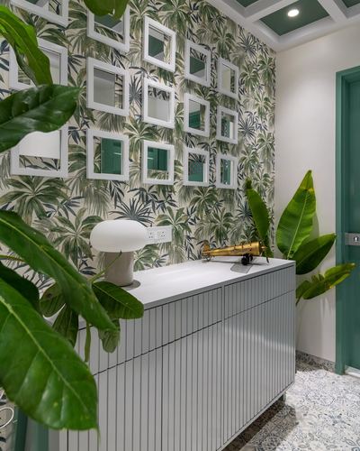 Foyer console with fluted cabinetry beneath a wall of mirrors on tropical wallpaper, framed by large green plants