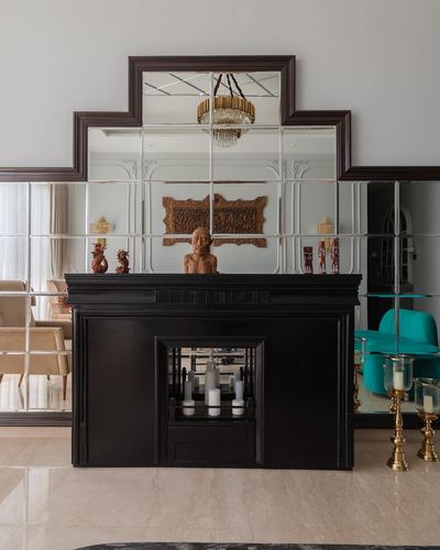 Black art deco fireplace beneath a stepped mirrored wall panel with a carved wooden bust and candle stands