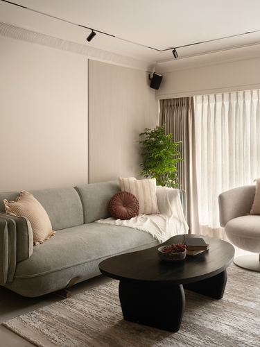 Beige living room with sage sofa, curved armchair, and black oval coffee table by sheer curtained window