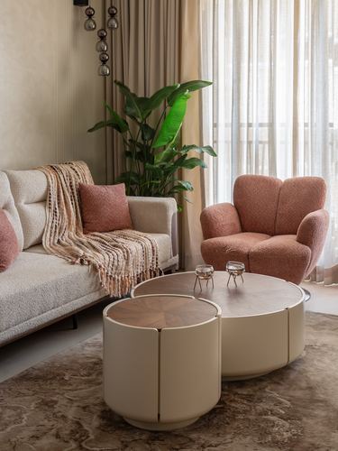 Living room with terracotta boucle armchair, beige sofa, and round wood-topped drum coffee tables