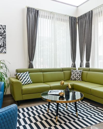Olive green corner sofa with black and white cushions beside floor-to-ceiling curtained windows