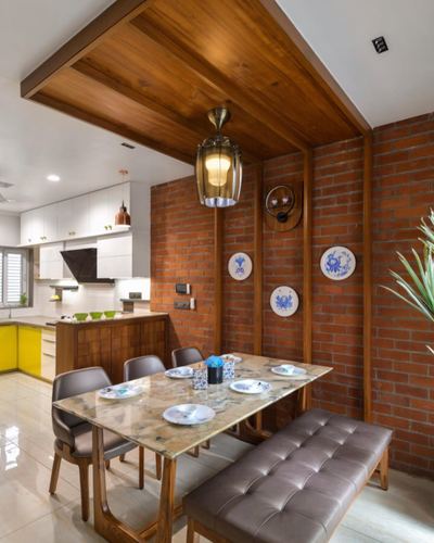 Dining area with marble table, leather bench, exposed brick wall and wood ceiling drop near open kitchen