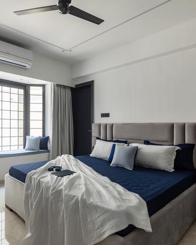Bedroom with grey channel-tufted headboard, navy bedding, white throw, and window seat nook.