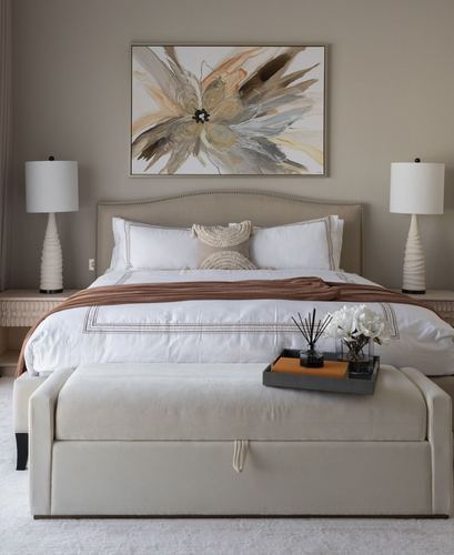 Neutral guest bedroom with upholstered headboard, twin lamps, abstract art, and a beige storage bench