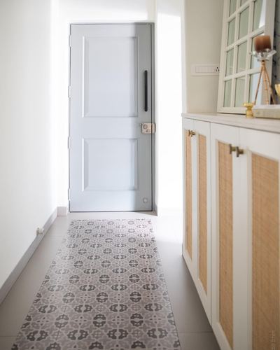 Narrow foyer with grey door, patterned tile runner, and cane-front cabinetry along the wall
