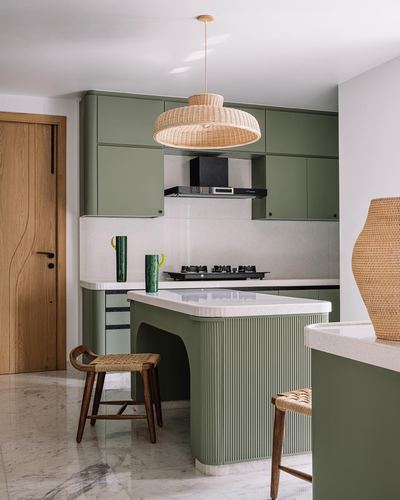 Sage green fluted kitchen island under a woven pendant light with cane stools and marble flooring