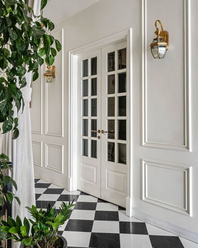 White paneled corridor with glass french doors, brass sconces, and black-white checkerboard marble floor