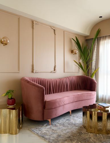 Pink velvet curved sofa against beige panelled wall with brass accents and a palm plant