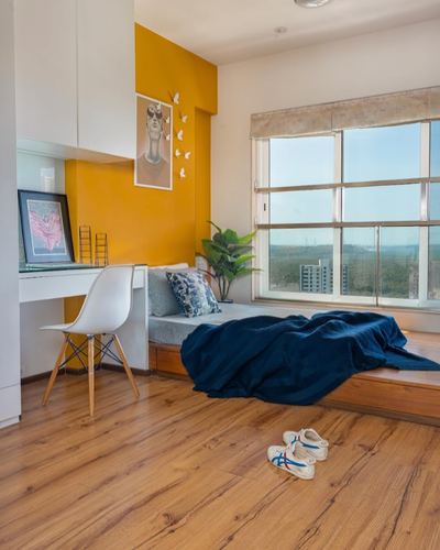 Sunlit bedroom nook with mustard wall, window seat, wooden floor, city view