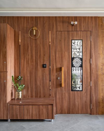 Wood-paneled entryway with a warli art glass door insert and a storage bench beside it