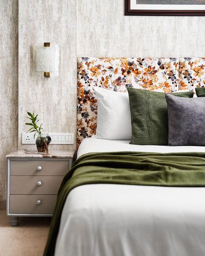 Bedroom corner with floral upholstered headboard, olive throw, marble-top nightstand and wall sconce