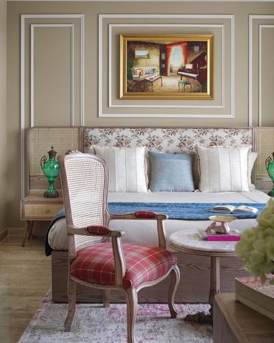 Bedroom corner with cane headboard bed, plaid armchair, framed painting and marble side table