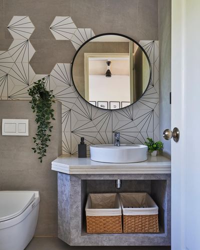 Round mirror over vessel sink with hexagonal patterned tile wall and woven baskets below