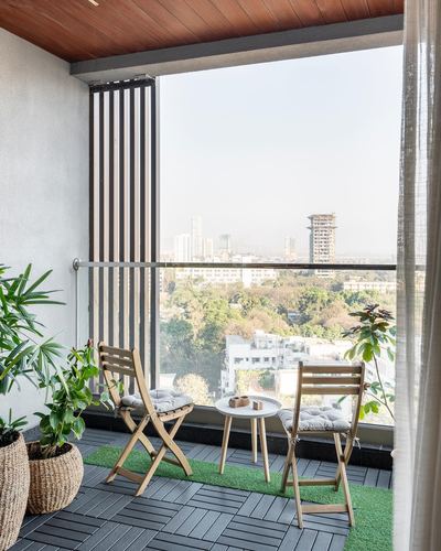 Balcony with two folding wooden chairs, round table, plants, and a distant city skyline view.