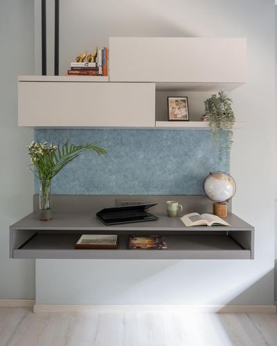 Floating grey desk under white cabinets with a blue textured backsplash panel and small decor items