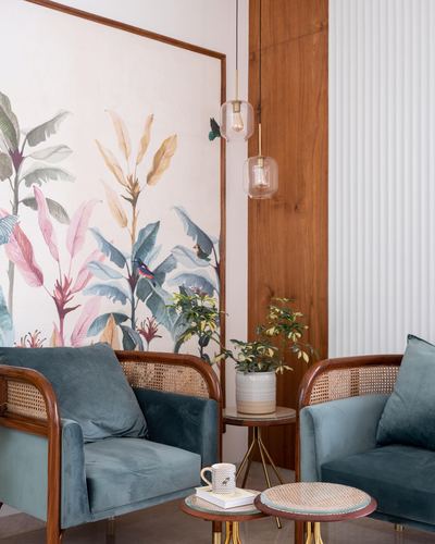 Teal velvet cane armchairs flank a plant-topped side table before a large botanical mural