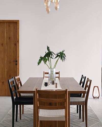 Wooden dining table with mixed chairs, palm plant centerpiece, pale wall behind
