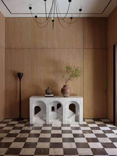 Foyer with wood paneled walls, checkerboard marble floor, sculptural arched marble console, and chandelier.